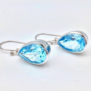 May include: A pair of silver teardrop earrings with light blue topaz gemstones.