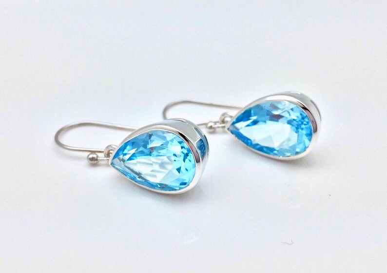 May include: A pair of silver teardrop earrings with light blue topaz gemstones.