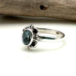 May include: A silver ring with a dark blue oval gemstone set in a decorative filigree design.