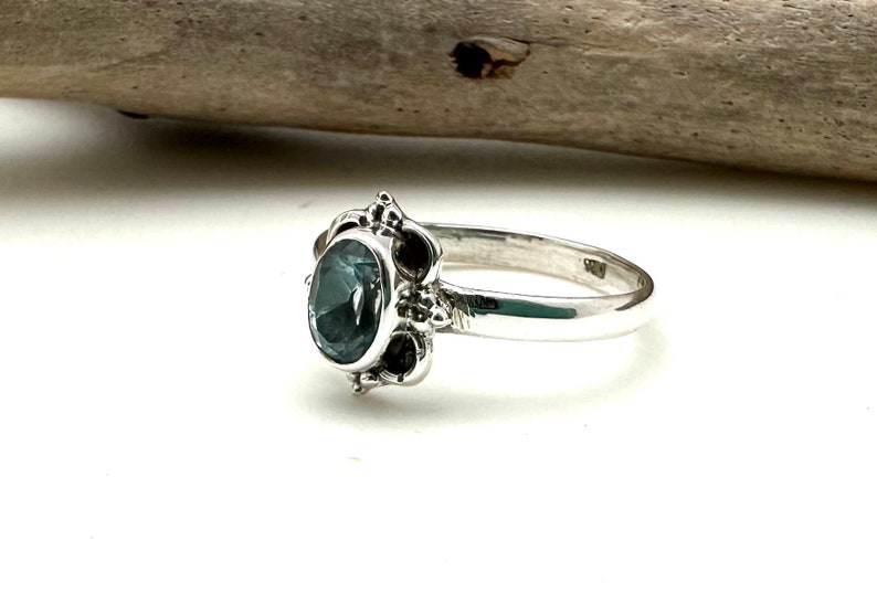 May include: A silver ring with a dark blue oval gemstone set in a decorative filigree design.