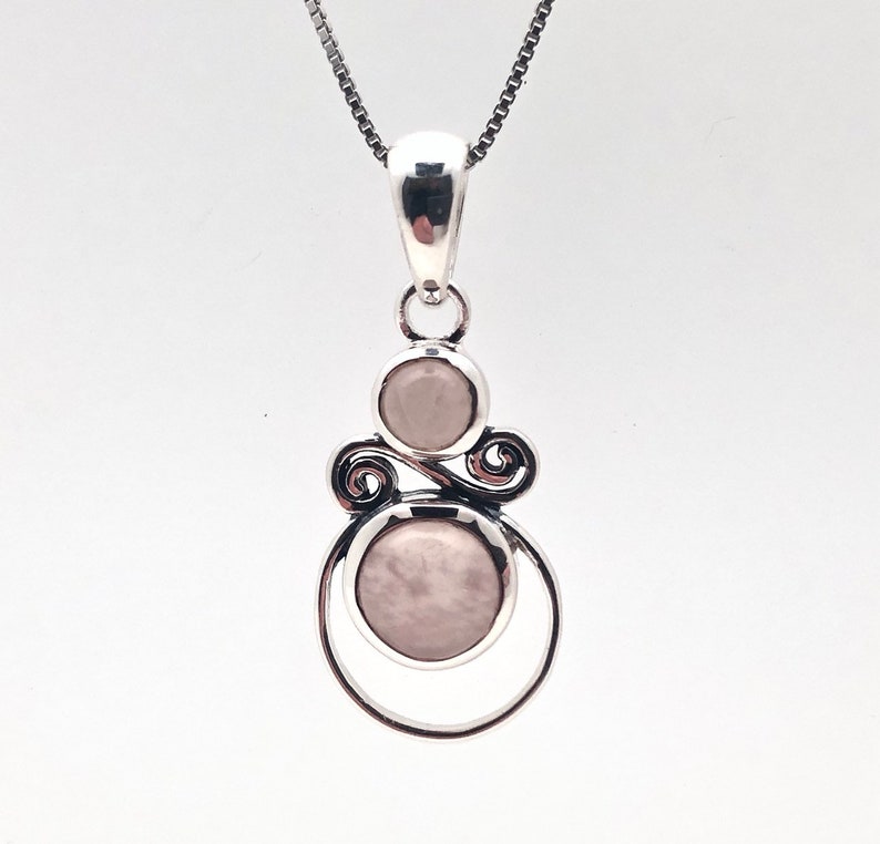 Peut inclure: Un collier avec un pendentif en argent orn&eacute; de deux pierres rondes rose p&acirc;le dans un motif argent&eacute; d&eacute;coratif.