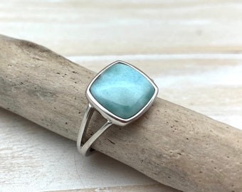 Può includere: Un anello d'argento con una pietra quadrata di colore blu chiaro. L'anello ha un design semplice ed elegante.
