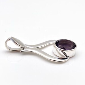 May include: A silver pendant featuring a purple gemstone. The pendant is shaped like a stylised heart with a bail at the top.