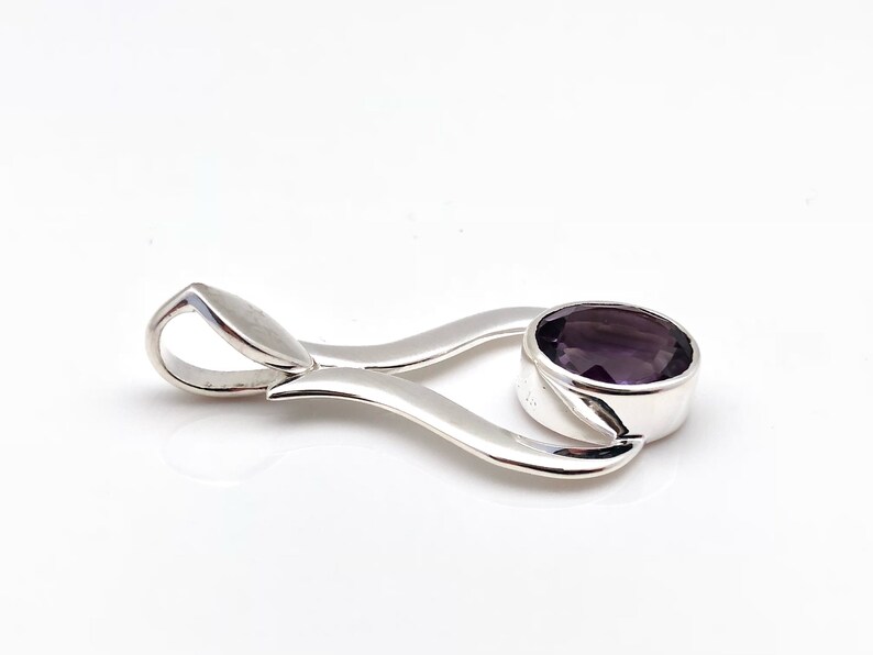 May include: A silver pendant featuring a purple gemstone. The pendant is shaped like a stylised heart with a bail at the top.