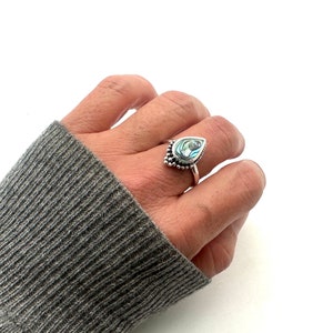 K&ouml;nnte beinhalten: Ein silberner Ring mit einem tropfenf&ouml;rmigen Abalone-Muschel-Stein. Der Ring hat ein Perlenmuster um den Stein.