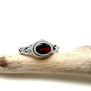 May include: A silver ring with an oval-shaped red gemstone set in a decorative filigree design.