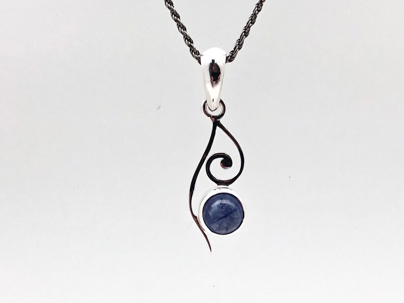 Op de afbeelding: Een zilveren ketting met een hanger met een blauwe edelsteen en een delicaat, zwierig ontwerp.