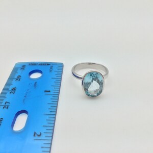 Pode incluir: Um anel de prata com uma gema oval azul claro. O anel est&aacute; ao lado de uma r&eacute;gua azul.