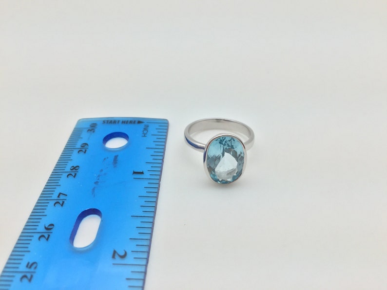Pode incluir: Um anel de prata com uma gema oval azul claro. O anel est&aacute; ao lado de uma r&eacute;gua azul.