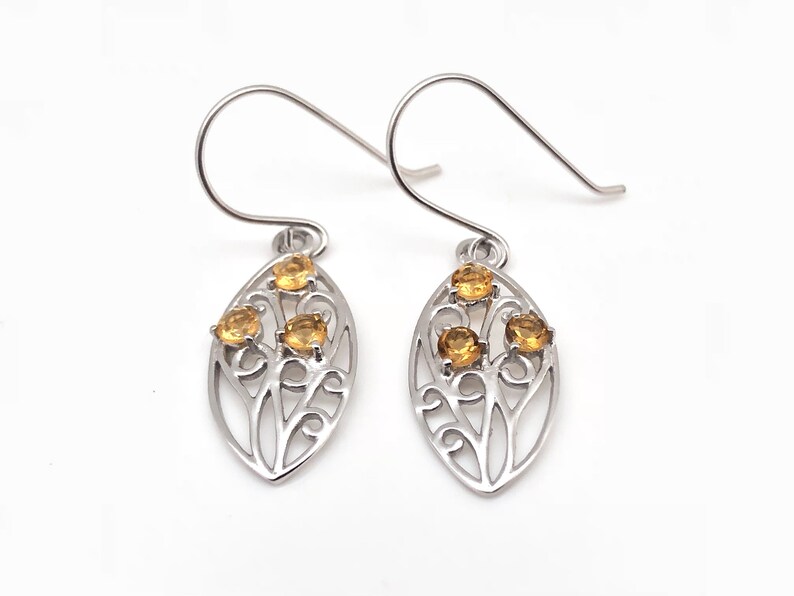 May include: A pair of silver earrings with a delicate leaf design and three small yellow gemstones.