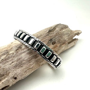May include: A silver bracelet with a braided design and black rectangular accents.