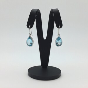 May include: A pair of silver teardrop earrings with light blue topaz gemstones.