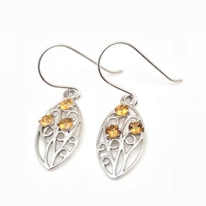 May include: Silver earrings with a delicate leaf design and three small yellow gemstones.