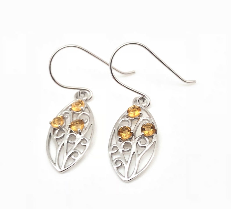 May include: Silver earrings with a delicate leaf design and three small yellow gemstones.