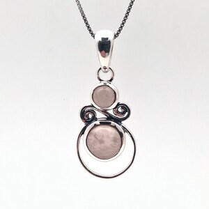 Peut inclure: Un collier avec un pendentif en argent avec deux pierres rondes rose p&acirc;le serties dans un motif en spirale.
