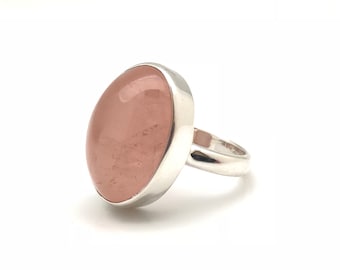 May include: A silver ring with a large oval-shaped pink gemstone.