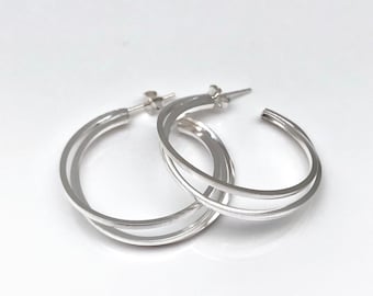 May include: Silver hoop earrings with a triple layered design. The hoops are smooth and polished.