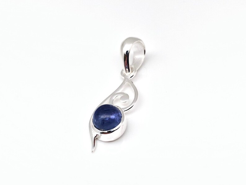 Op de afbeelding: Een zilveren hanger met een blauwe edelsteen in een swirl-ontwerp.