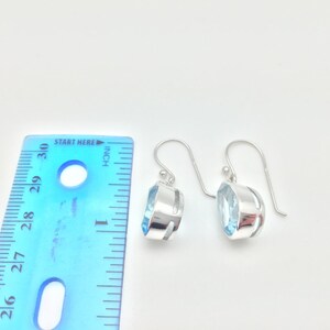 May include: A pair of silver dangle earrings with light blue gemstone accents. The earrings are approximately 1 inch long.