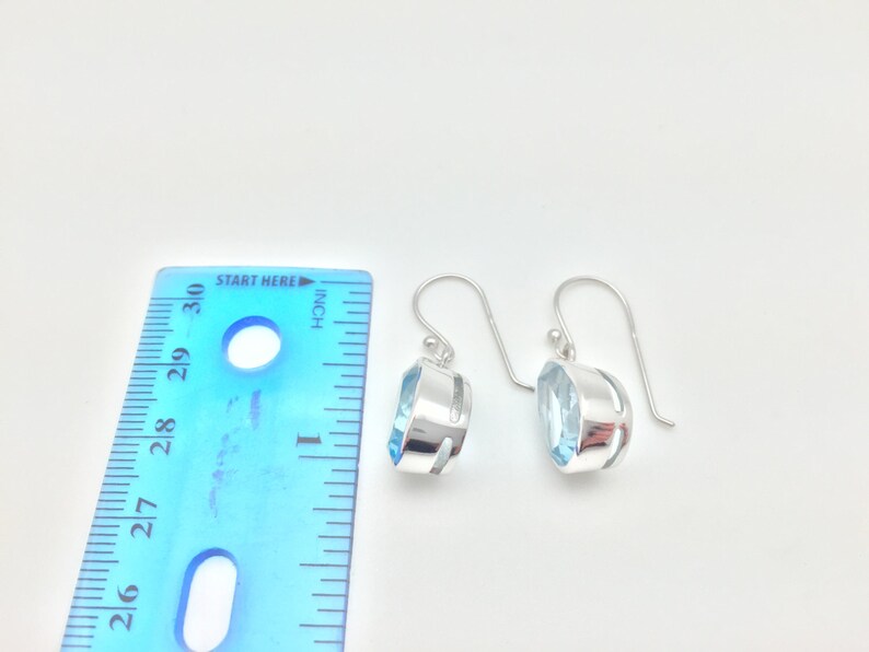 May include: A pair of silver dangle earrings with light blue gemstone accents. The earrings are approximately 1 inch long.