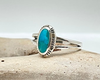 May include: A silver ring with a turquoise oval stone set in a silver bezel. The ring has a double band.