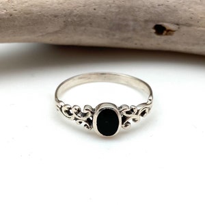 May include: A silver ring featuring a black oval stone set in a delicate filigree design.