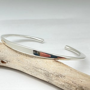 May include: A simple silver bangle bracelet with a smooth, rounded finish.
