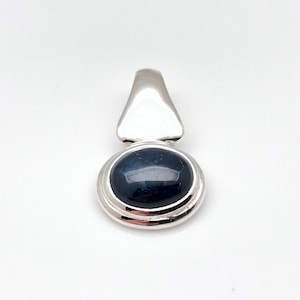 Op de afbeelding: Een zilveren hanger met een ronde, donkerblauwe edelsteen gezet in een dubbele rand.