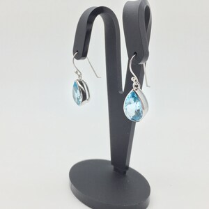 May include: A pair of silver teardrop earrings with light blue topaz gemstones.