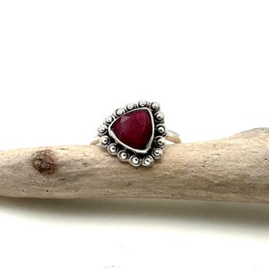 May include: A silver ring with a triangular red gemstone set in a beaded bezel.