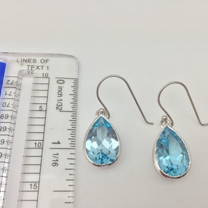 Puede incluir: Un par de pendientes de plata en forma de l&aacute;grima con piedras preciosas azul claro. Los pendientes miden aproximadamente 1,25 cm de largo.
