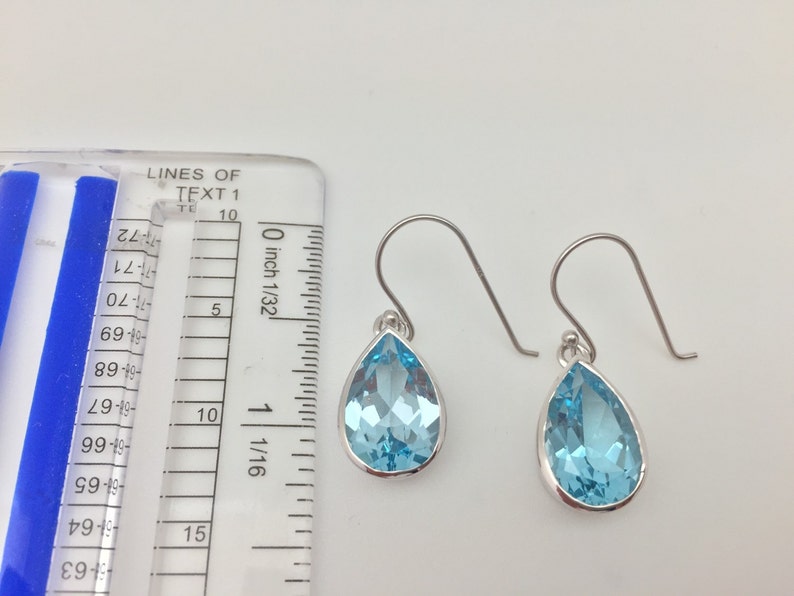 Puede incluir: Un par de pendientes de plata en forma de l&aacute;grima con piedras preciosas azul claro. Los pendientes miden aproximadamente 1,25 cm de largo.