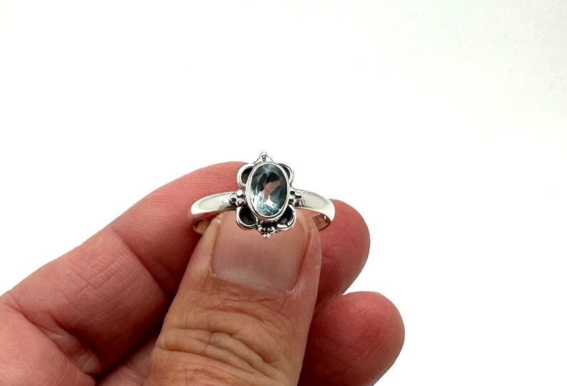 May include: A silver ring with a light blue oval gemstone set in a floral design.
