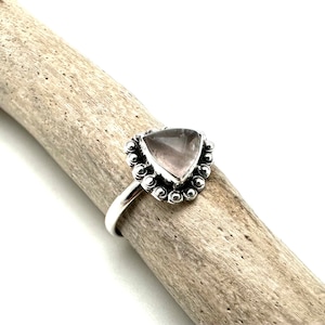 May include: A silver ring with a triangular pink gemstone set in a beaded bezel.