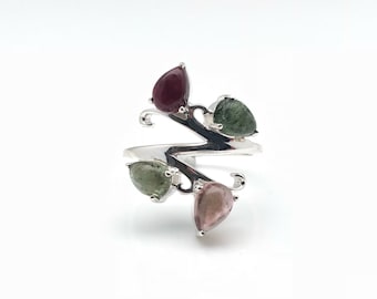 May include: A silver ring with a swirling design featuring four teardrop-shaped gemstones. The gemstones are green, pink, and red.