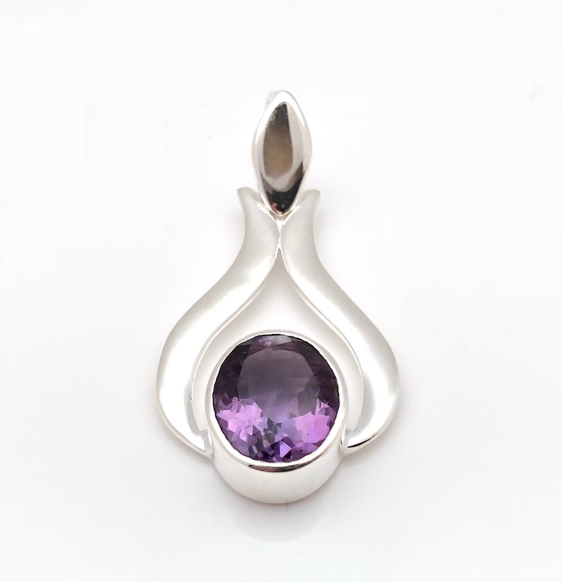 May include: A silver pendant featuring a purple amethyst gemstone. The pendant has a distinctive, flowing design.