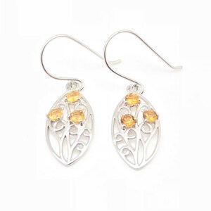 May include: Silver earrings with a delicate filigree design and three small, round, yellow gemstones.