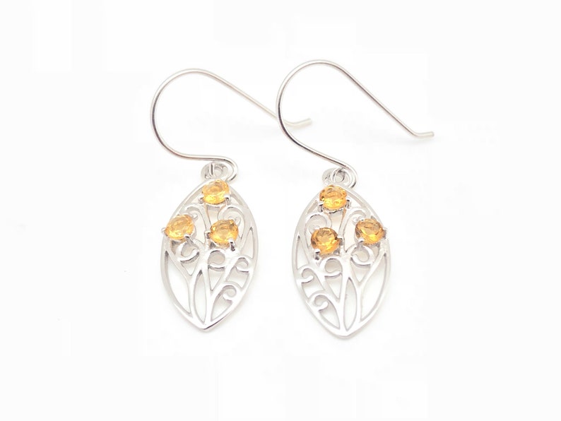 May include: Silver earrings with a delicate filigree design and three small, round, yellow gemstones.