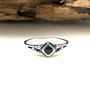 May include: A silver ring featuring a black gemstone set in a square shape. The ring has a delicate design with small beads around the gemstone.