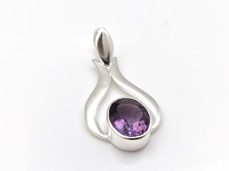 May include: A silver pendant featuring a purple amethyst gemstone set in a delicate, flowing design.