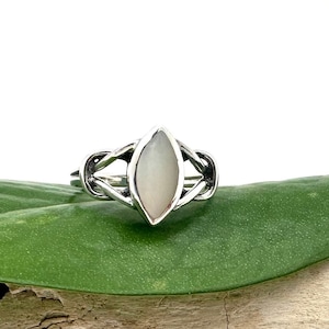 May include: A silver ring with a white mother of pearl oval stone set in a Celtic knot design.