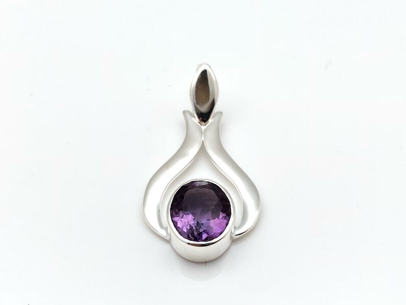 May include: A silver pendant featuring a purple amethyst gemstone set in a delicate, curved design.