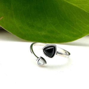 May include: A silver ring with a black triangle-shaped stone and a white triangle-shaped stone. The ring is open and adjustable.