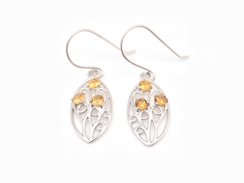 May include: A pair of silver earrings with a delicate leaf design and four small yellow gemstones.