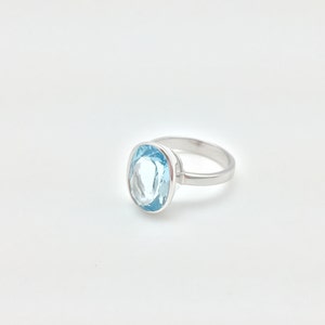 Pode incluir: Um anel de prata com uma pedra oval de cor azul claro.
