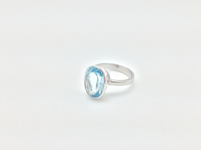 Pode incluir: Um anel de prata com uma pedra oval de cor azul claro.