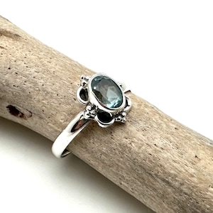 May include: A silver ring with a blue oval gemstone set in a decorative silver setting.