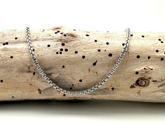 Op de afbeelding: Een zilveren ketting met een box chain-ontwerp. De ketting ligt op een stuk drijfhout.