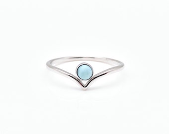 May include: A silver-toned V-shaped ring featuring a single, small, round, light blue cabochon stone set at the center point of the band. The metal band has a smooth, polished finish and a delicate, thin profile that tapers toward the back.