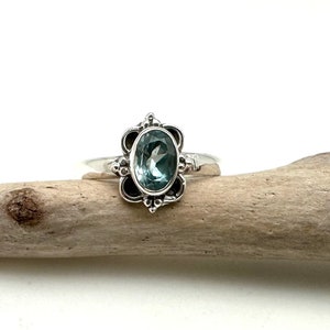 May include: A silver ring with a light blue oval gemstone set in a floral design.